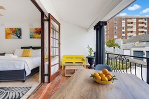 A balcony with a bed, a yellow bench, a table with a bowl of fruit, and a potted plant. - The Sea Point Treat Balcony & Lion’s Head Views (Cape Town)