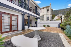 A courtyard with a white stone fountain, a door with glass panels, and a balcony with black railings. - The Sea Point Treat Balcony & Lion’s Head Views (Cape Town)