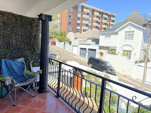 A balcony with a chair and a table, overlooking a street with parked cars and buildings. - The Sea Point Treat Balcony & Lion’s Head Views (Cape Town)