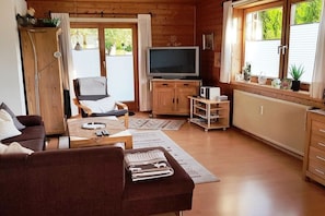 A cozy living room with a sofa, a television, and a dining area. - Alpine garden in the holiday home Weimar (Ellmau)
