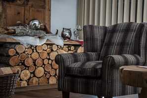 Ein Wohnzimmer mit einem Karoknock-Sessel, einem Holztisch und einem Kamin mit brennendem Holz.