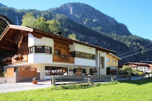A two-story building with a balcony, a wooden fence, and a mountain backdrop. - Holiday apartment with 2 bedrooms (Umhausen)