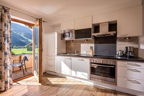 Een moderne keuken met uitzicht op een bergachtig landschap door een open deur.