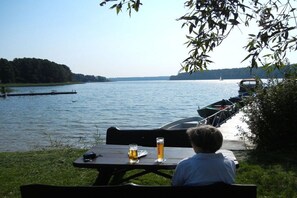 A lakeside setting with a table and chairs, two glasses of beer, and a boat docked in the background. - Holiday home with 1 bedroom (Alt-Schwerin)