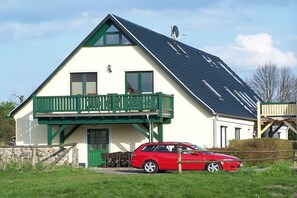 Ein zweistöckiges Haus mit Balkon, ein Auto vor der Tür und ein klarer Himmel.