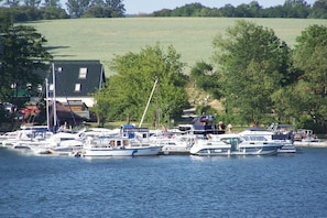 Ein Hafen mit mehreren angestoßenen Booten, umgeben von Bäumen und einem Gebäude mit grüner Dachbegrünung.