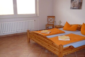 Ein hölzernes Bett mit orangefarbener Bettwäsche, ein Sessel, ein Nachttisch mit Lampe und eine Heizung.