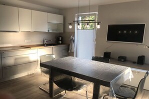 Eine moderne Küche mit Esstisch, Stühlen, einer Kaffeemaschine und einem an der Wand befestigten Fernseher.