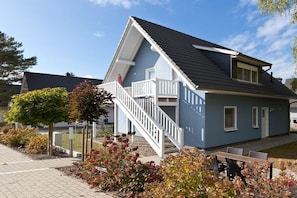 Ein zweistöckiges Haus mit Balkon, einer Treppe und einem Garten mit Herbstlaub.