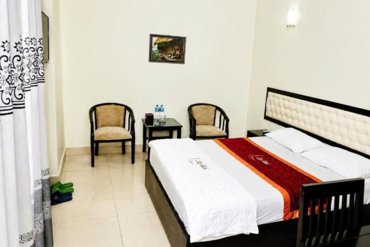 A hotel room with a bed, two chairs, a small table, and a picture on the wall.