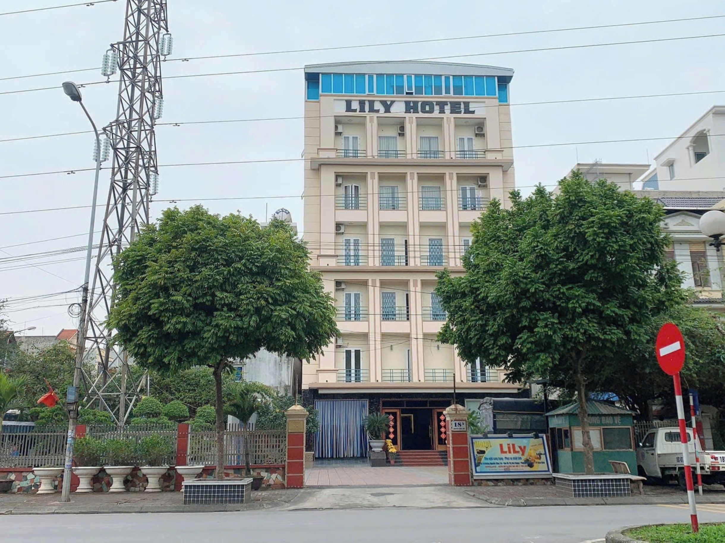 A multi-story hotel named 'Lily Hotel' with a prominent entrance, a gated driveway, and a signboard advertising the hotel.