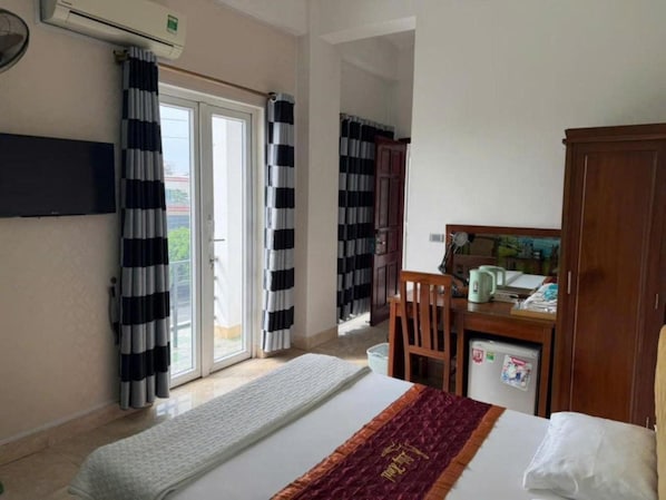 A hotel room with a bed, a desk with a chair, a wardrobe, and a television mounted on the wall.