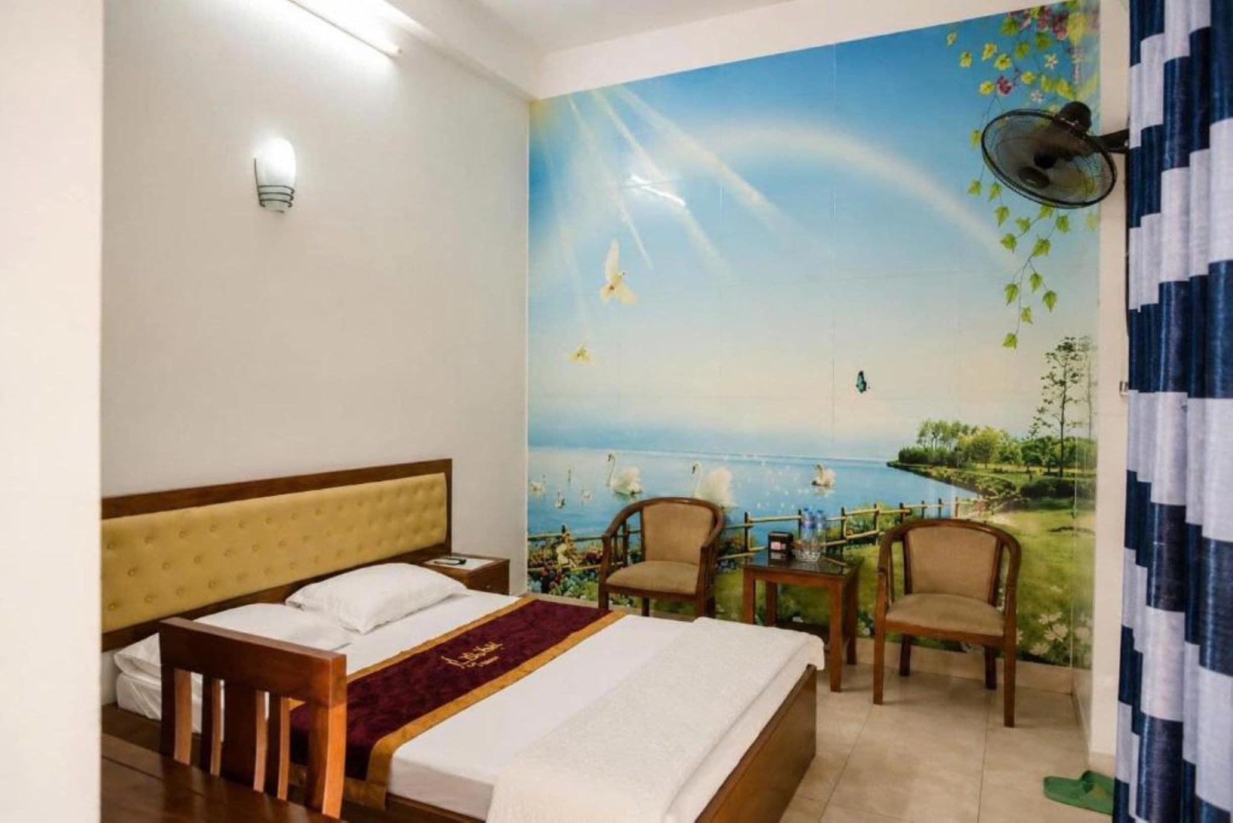 A hotel room with a bed, two chairs, a small table, and a mural of a landscape with birds.