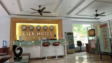 A hotel reception area with a modern design, featuring a reception desk, seating area, and a wall with clocks indicating different cities.