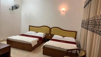 A hotel room with two beds, a bedside table, a chair, and a wall-mounted fan.