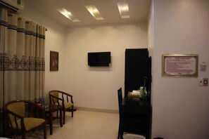 A hotel room with a bed, a desk, a chair, a television, and a wall-mounted sign.