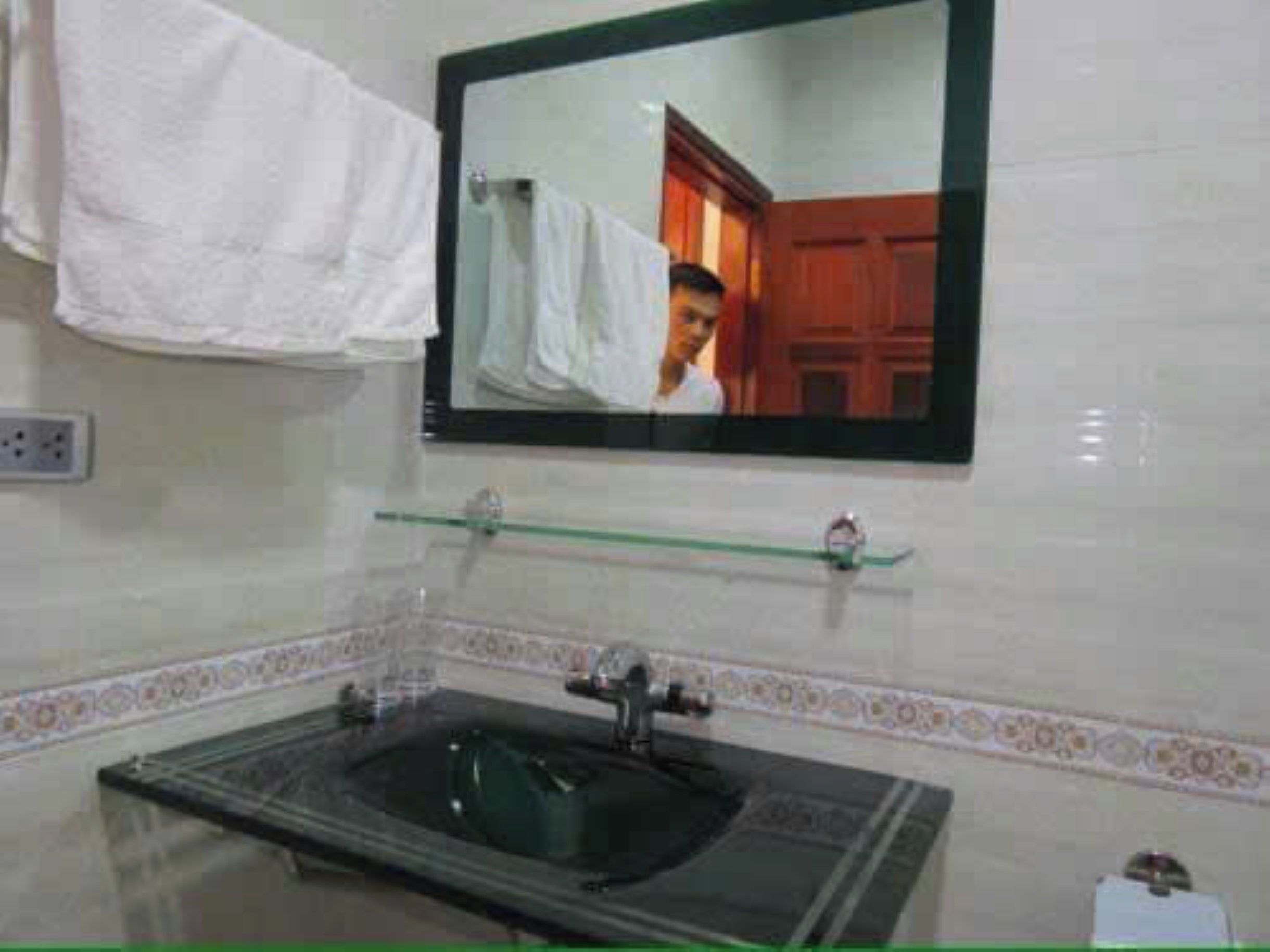 A bathroom with a glass sink, a mirror, and a towel hanging on the wall.