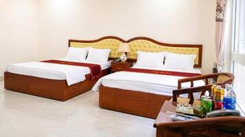 A hotel room with two beds, a wooden headboard, a nightstand, a lamp, and a small table with a chair.
