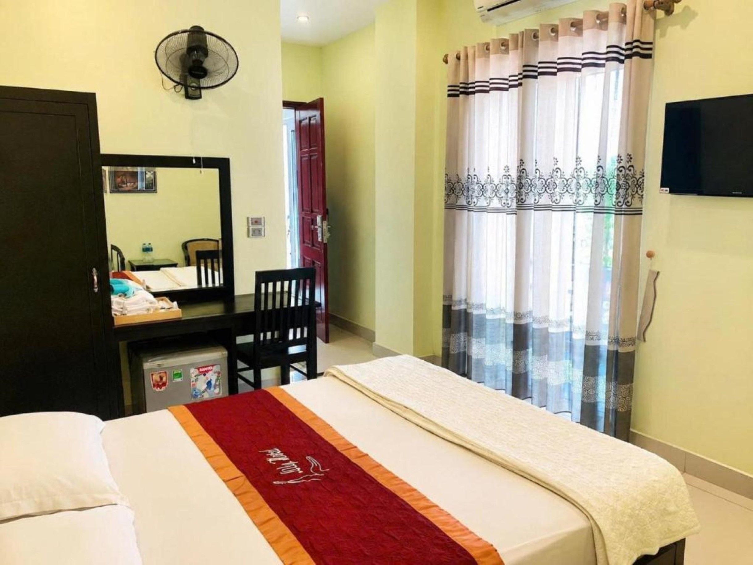 Ein Hotelzimmer mit Bett, Schreibtisch, Stuhl, Spiegel und Fernseher.