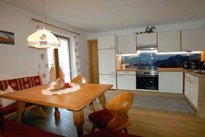 Eine kleine Küche mit weißen Schränken, einem Holztisch und Bergblick durch das Fenster.