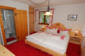 A bedroom with a wooden bed, a window with curtains, a bedside table with a lamp, and a wooden wardrobe. - Maple view in the Tasser house (Mayrhofen)