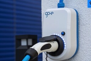 Een laadstation voor elektrische voertuigen met een wit en blauw ontwerp, een oplaadkabel en een blauwe indicatorlamp.