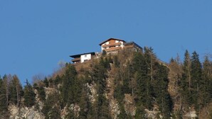 A multi-story building with a flat roof, situated on a hill surrounded by dense forest. - Maple view in the Tasser house (Mayrhofen)