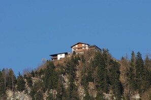A multi-story building with a flat roof, situated on a hill surrounded by dense forest. - Maple view in the Tasser house (Mayrhofen)