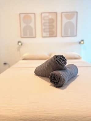 A neatly made bed with two rolled towels on top, a bedside table with a lamp, and three framed pictures on the wall. - Corporate 90+Day | 2BR&2BA | Travel Professionals (Surrey)