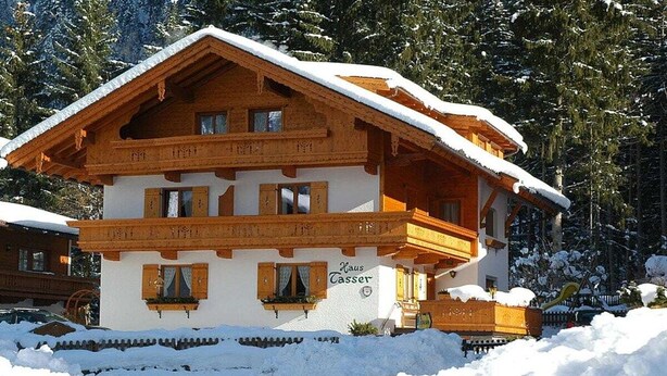 A two-story wooden chalet with a snow-covered roof, surrounded by trees and a snow-covered ground. - Penkenblick in the Tasser House (Mayrhofen)