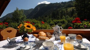 A breakfast table set with a pitcher, teapot, cups, saucers, a bowl of bread, a vase with flowers, and a glass of orange juice. - Penkenblick in the Tasser House (Mayrhofen)