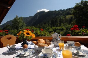 A breakfast table set with a pitcher, teapot, cups, saucers, a bowl of bread, a vase with flowers, and a glass of orange juice. - Penkenblick in the Tasser House (Mayrhofen)
