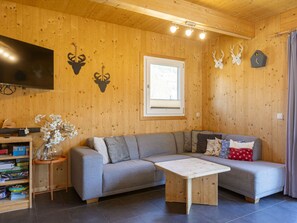 Ein modernes Wohnzimmer mit einem grauen Ecksofa, einem Holztisch und einem an der Wand montierten Fernseher.