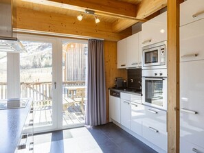 Eine moderne Küche mit Holzbalken an der Decke, einer Glastür, die zu einer Terrasses führt, und Edelstahlgeräten.