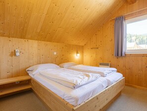 Ein Zimmer aus Holz mit einem Bett, einem Fenster mit Vorhängen und einer Wandleuchte.