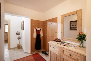 A hotel room with a wooden wardrobe, a mirror, a red rug, and a small table with shoes and a vase of flowers. - Kolm in Christina's country house (Mayrhofen)