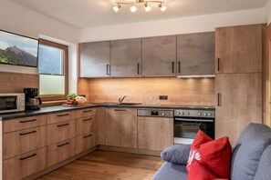 A modern kitchen with wooden cabinets, a built-in oven, and a window with a mountain view. - Kolm in Christina's country house (Mayrhofen)
