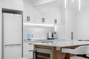 A modern kitchen with white cabinetry, a marble backsplash, and a central island with a wooden countertop. - Jindiburra Coastal Haven at Noosaville (Noosaville)