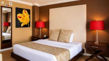 Habitación de hotel con una cama grande, dos mesitas de noche con lámparas, un espejo y un cuadro en la pared.