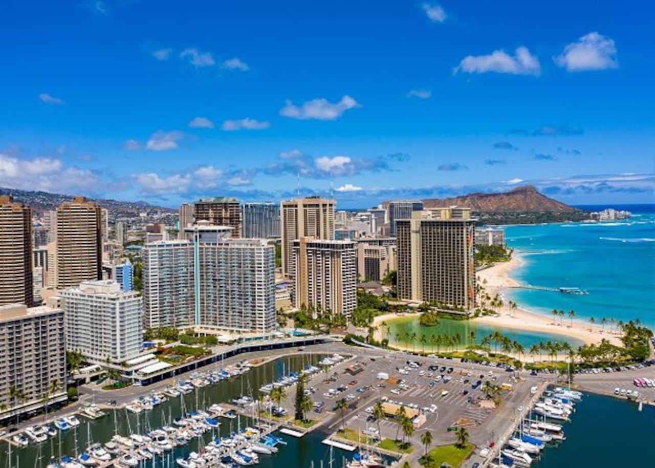A coastal cityscape with high-rise buildings, a marina, and a beach.