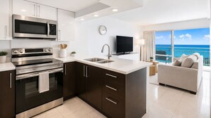 Una cocina moderna con microondas, horno y lavabo integrados, un televisor de pantalla plana y un balcón con vistas al océano.