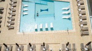 Una piscina rectangular con un trampolín y múltiples sillas de descanso alrededor.