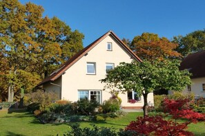 A two-story house with a sloped roof, a front porch, and a well-maintained garden with various plants and trees. - Holiday apartment with 2 bedrooms (Ostseebad Heringsdorf)