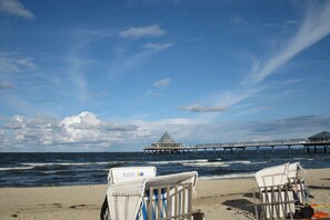 A beach with two wicker chairs, a pier, and a building in the distance. - Holiday apartment with 2 bedrooms (Ostseebad Heringsdorf)