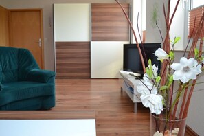 Una sala de estar con un sofá color turquesa, un televisor de pantalla plana y un jarrón decorativo con flores blancas.