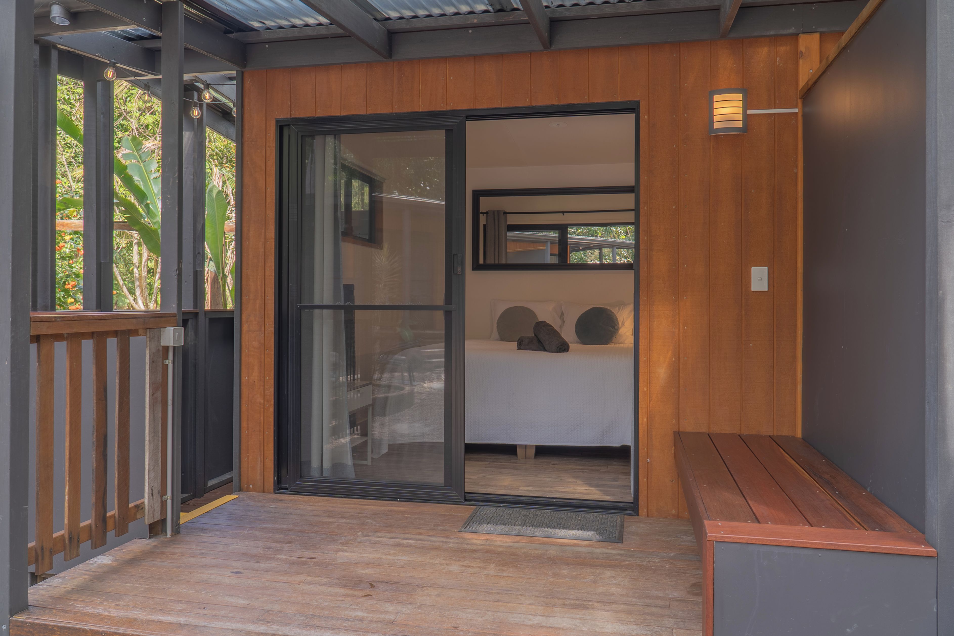 A modern room with a sliding glass door leading to a balcony, a bed with pillows, and a bench.