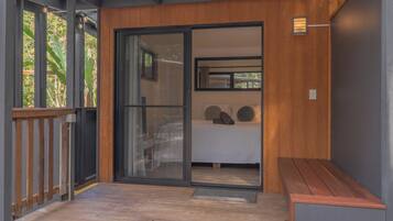 A modern room with a sliding glass door leading to a balcony, a bed with pillows, and a bench.