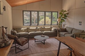 A modern living room with a sofa, a coffee table, and a wooden table. - Private Hinterland Cabin near Beaches & Rail Trail: Cabin 2 (Burringbar)