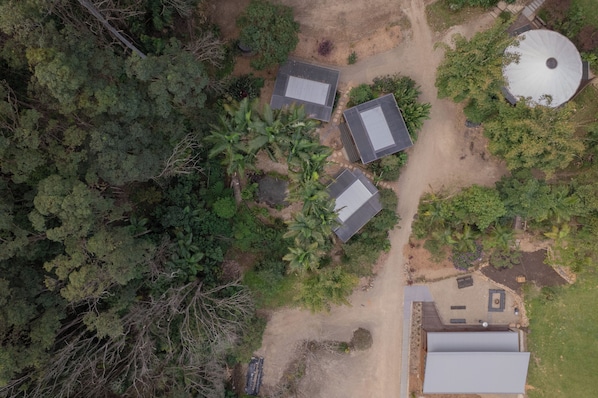 An aerial view of a residential area with multiple houses, a large circular structure, and surrounding greenery. - Private Hinterland Cabin near Beaches & Rail Trail: Cabin 2 (Burringbar)