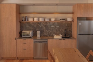 A modern kitchen with wooden cabinets, a built-in dishwasher, a stainless steel refrigerator, and a marble backsplash.